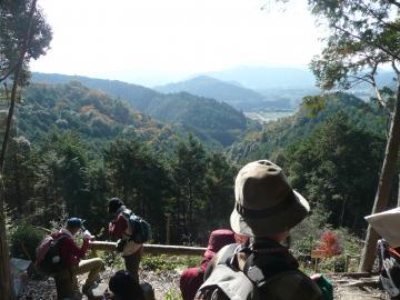 登山者が休憩している高い場所から、山並みと遠くの景色を写している写真